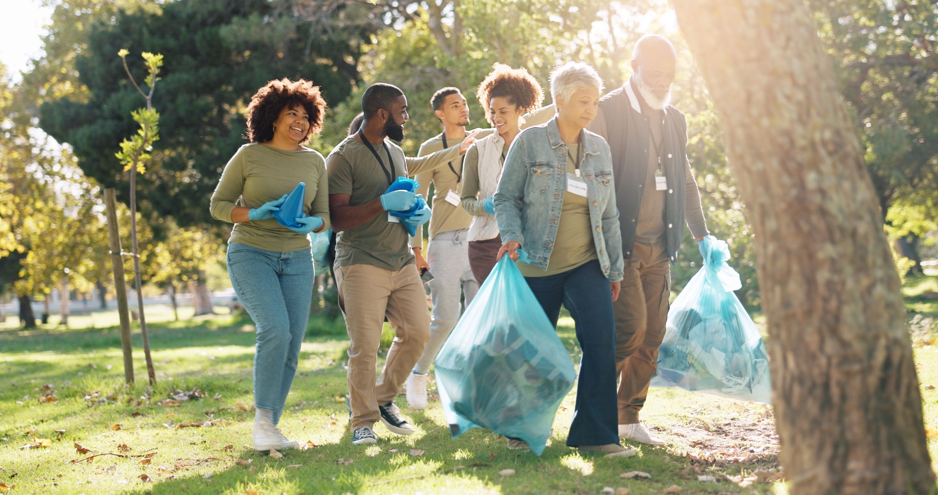 People, volunteer and smile for pick up dirt at park with plastic bag for cleaning, earth day and community service. Outdoor, litter and waste collection for maintenance, environment and charity work